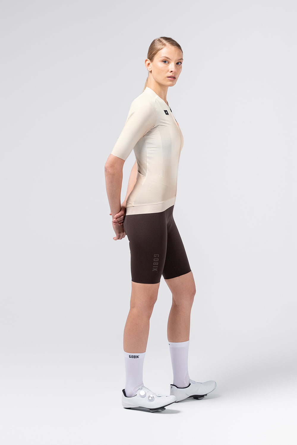 Female model wearing Gobik CX Pro 4.0 almond jersey with dark brown cycling shorts, side view