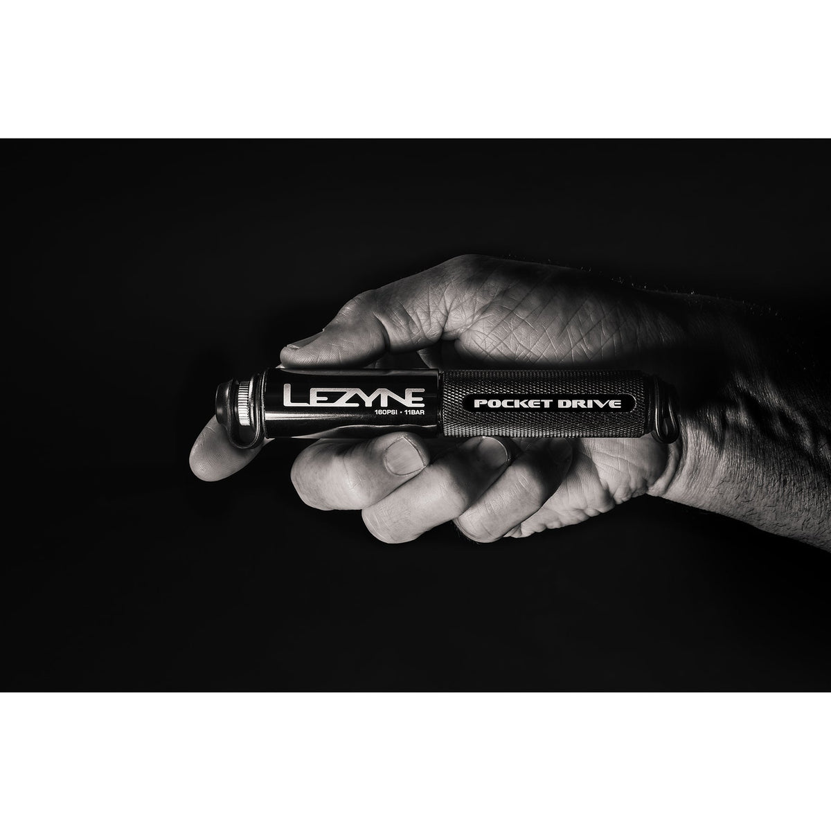 Hand holding Lezyne Pocket Drive mini bike pump in dramatic black and white studio photo