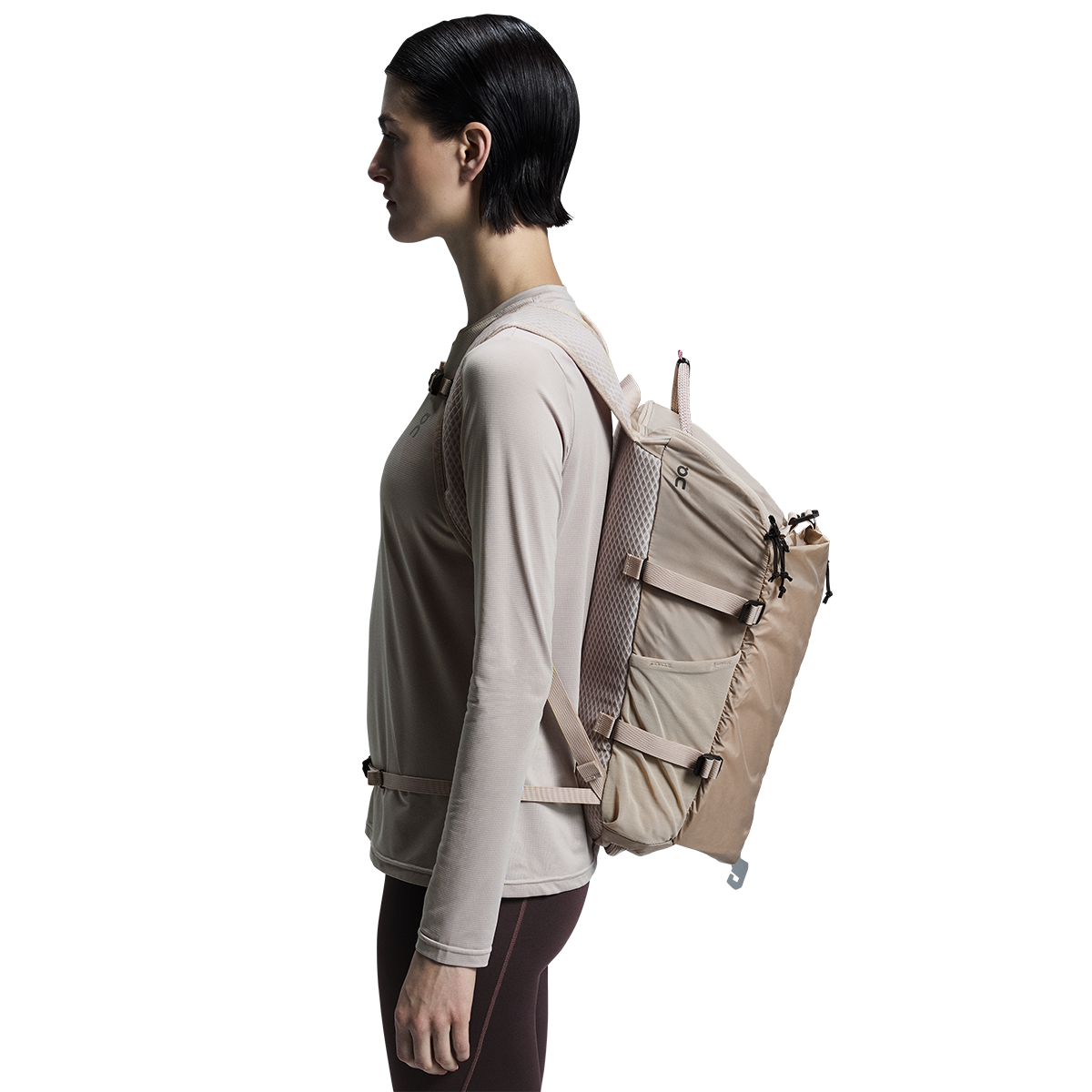 Woman wearing On Speed Pack 18L Lite backpack in cream sand color, side profile view