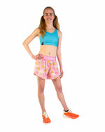Woman wearing pink ChicknLegs split shorts with yellow tiara pattern and blue sports bra