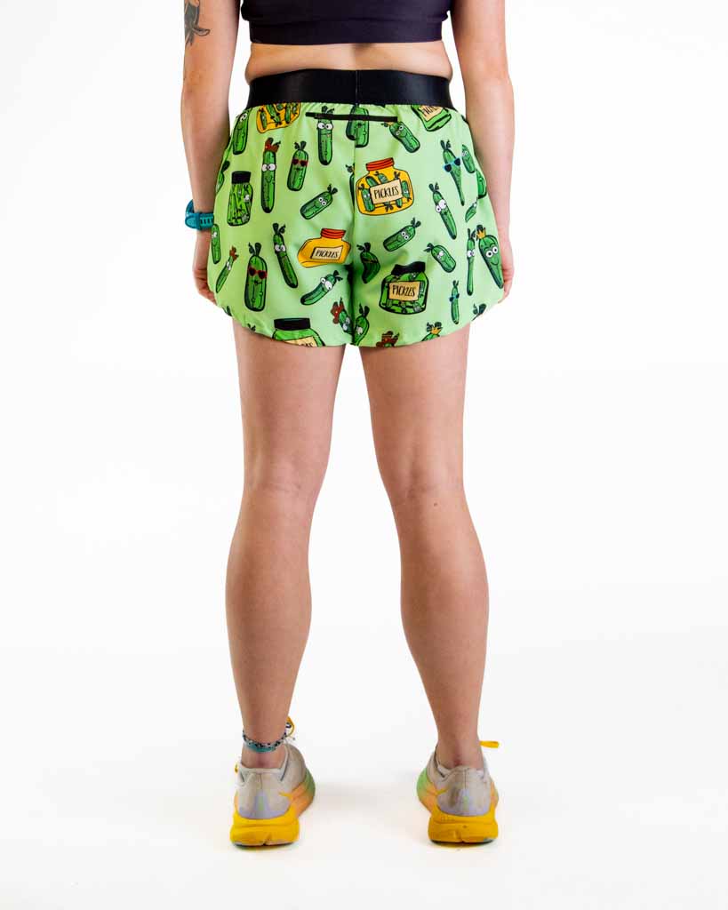 Woman wearing green pickle-patterned split running shorts, back view on white background