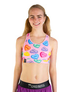 ChicknLegs OG Sports Bra in pink Candy Hearts print worn by smiling female model