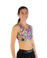 Woman wearing ChicknLegs tie-dye sports bra in vibrant rainbow colors with black leggings