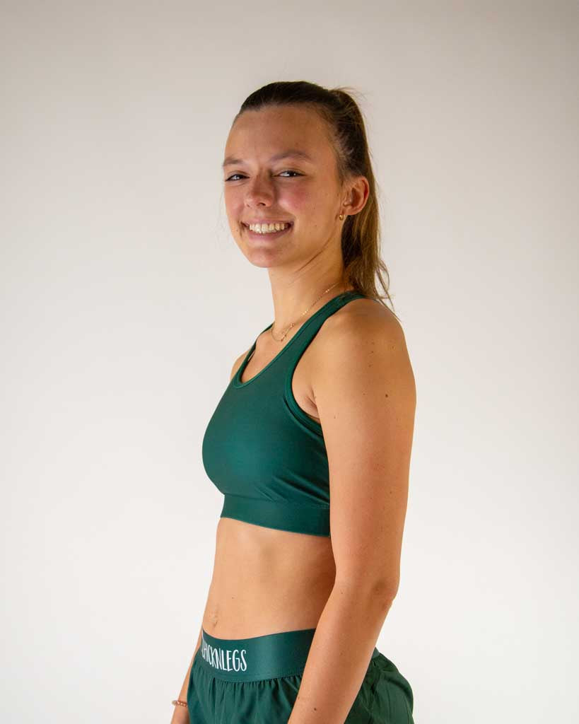 Woman wearing forest green ChicknLegs sports bra and matching shorts, smiling
