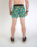 Man wearing teal blue shorts with orange dinosaur nugget pattern from behind