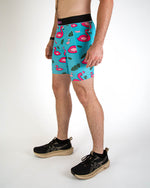 Man wearing turquoise blue shorts with pink flamingo pattern and tropical leaf design