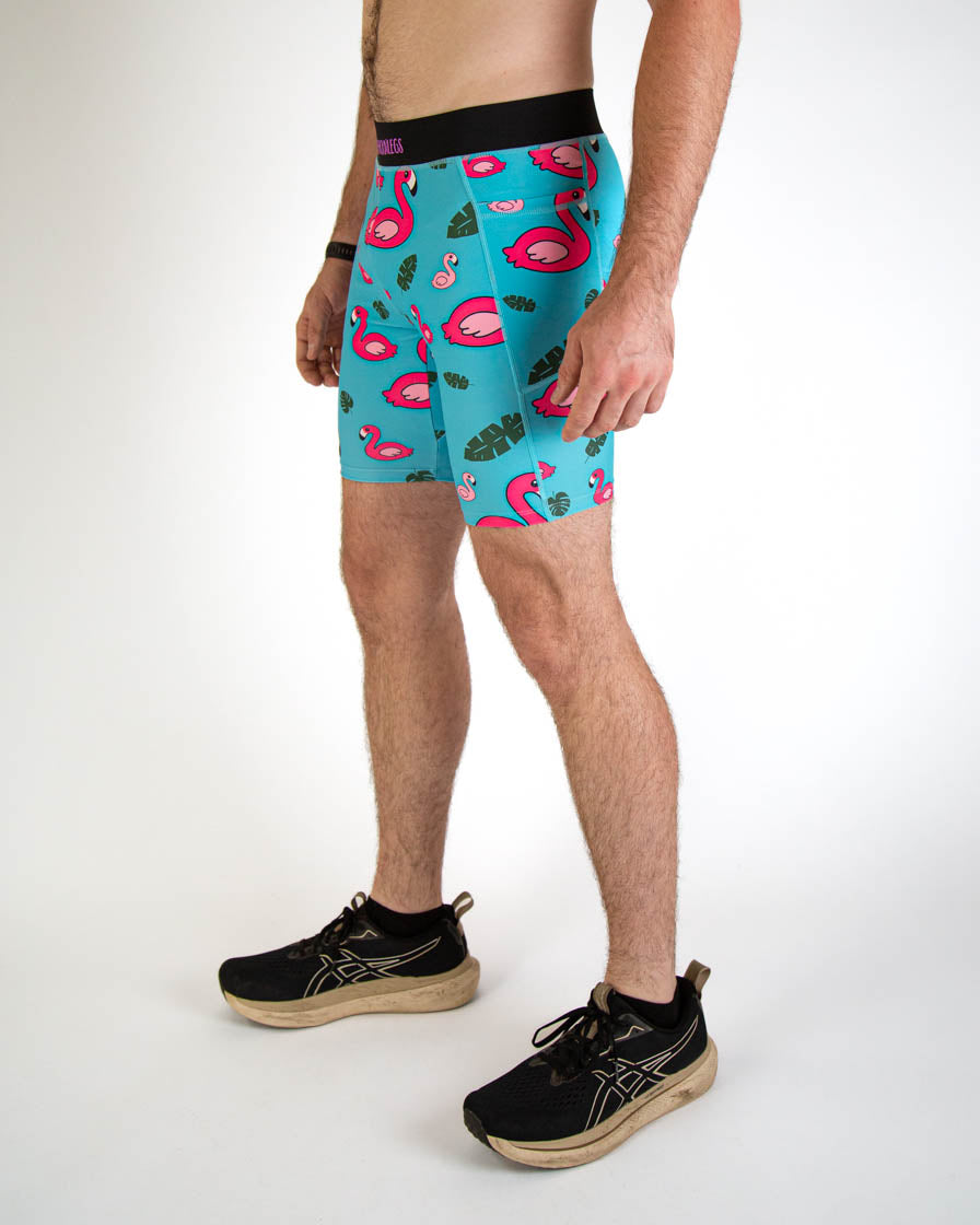 Man wearing turquoise blue shorts with pink flamingo pattern and tropical leaf design