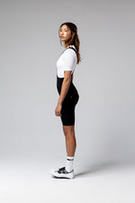 Woman wearing black Gobik Ultralite bib shorts with white top and cycling shoes