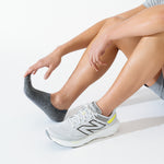 Person putting on gray Feetures Elite Light Cushion Invisible no-show sock with New Balance shoe