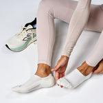 Person putting on white Feetures Elite Light Cushion Invisible no-show socks with New Balance sneaker nearby