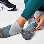 Person wearing Feetures Elite Light Cushion Tab socks in Stone Ivy colorway with teal leggings