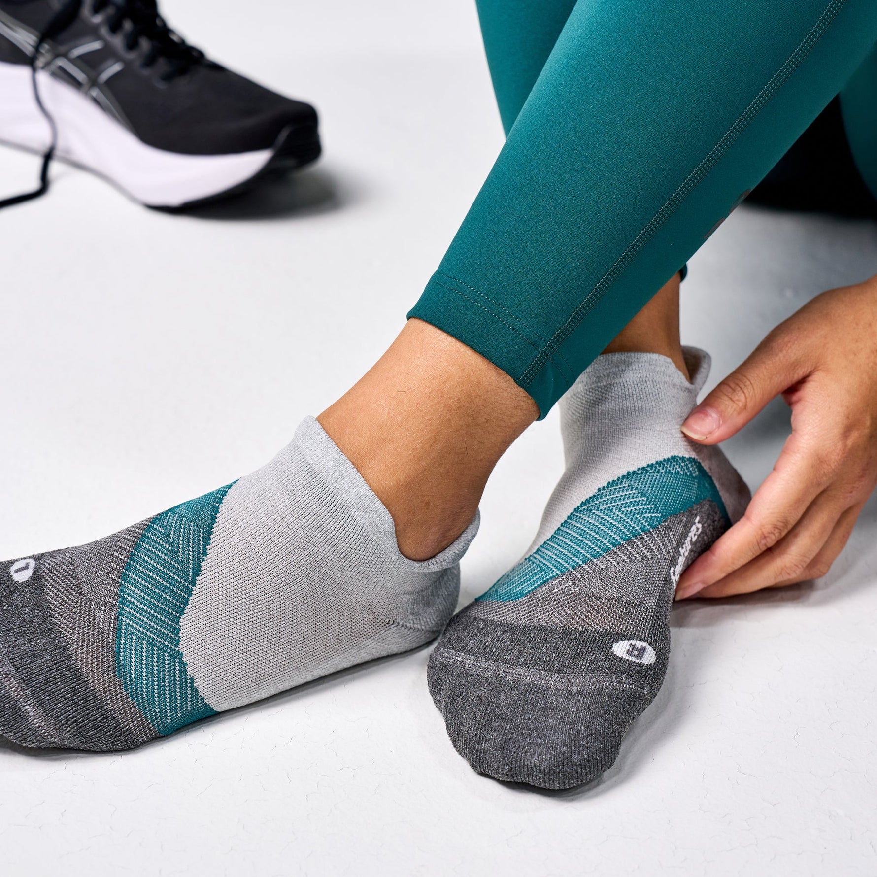 Person wearing Feetures Elite Light Cushion Tab socks in Stone Ivy colorway with teal leggings