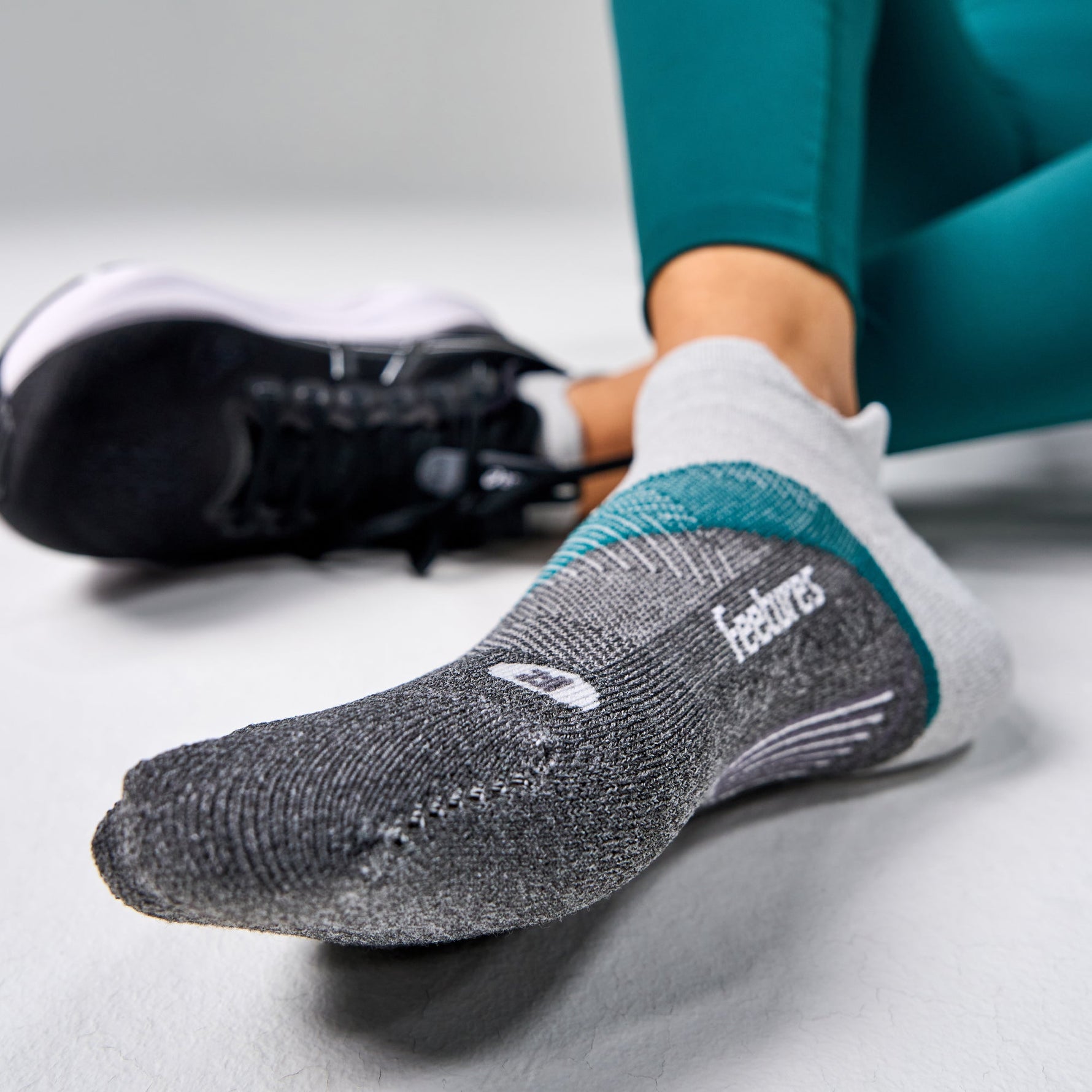 Feetures Elite Light Cushion Tab sock in Stone Ivy shown on foot with running shoe nearby