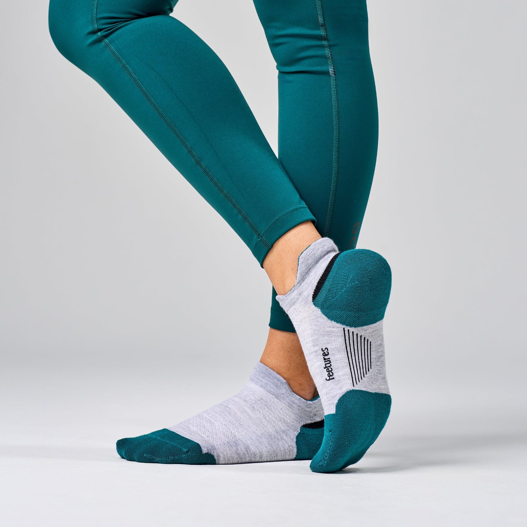 Feetures Elite Max Cushion Tab socks in white with teal accents worn with athletic leggings