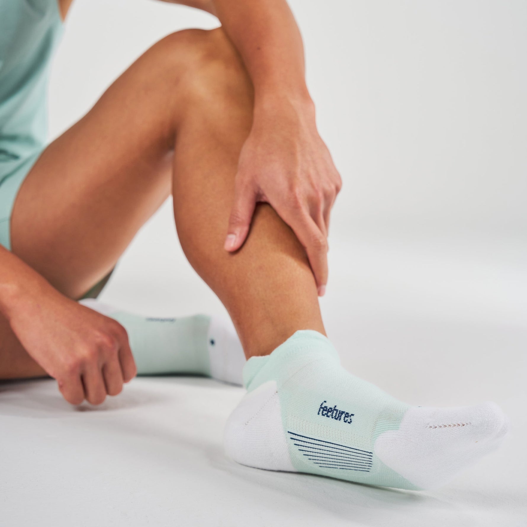 Person wearing Feetures Elite Max Cushion Tab socks in white and mint green colorway