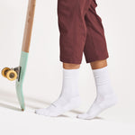 Person wearing white Feetures High Performance Max Cushion Crew socks with skateboard nearby