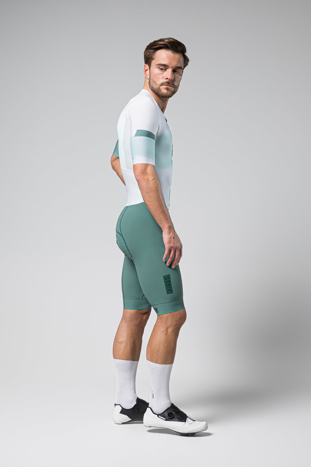 Male model wearing Gobik Brooklyn Aerosuit in sage green cycling outfit with white accents