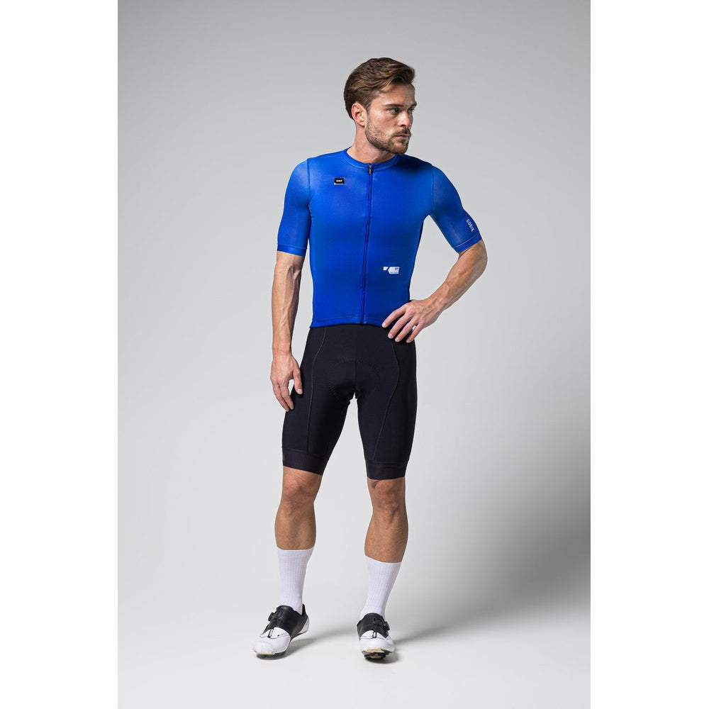 Male cyclist wearing blue Gobik Stark jersey with black shorts in studio setting