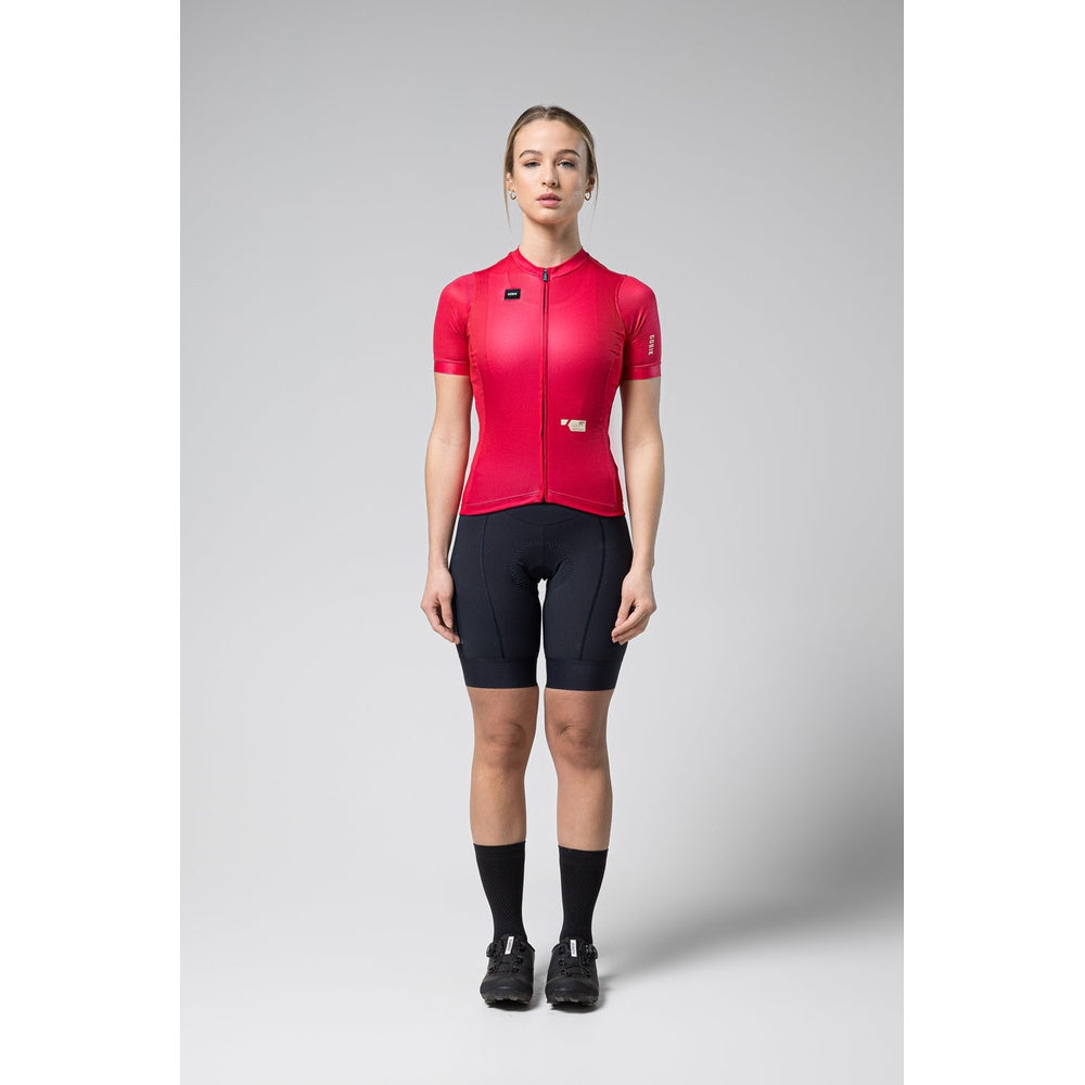 Woman wearing bright pink Gobik Stark cycling jersey with black shorts