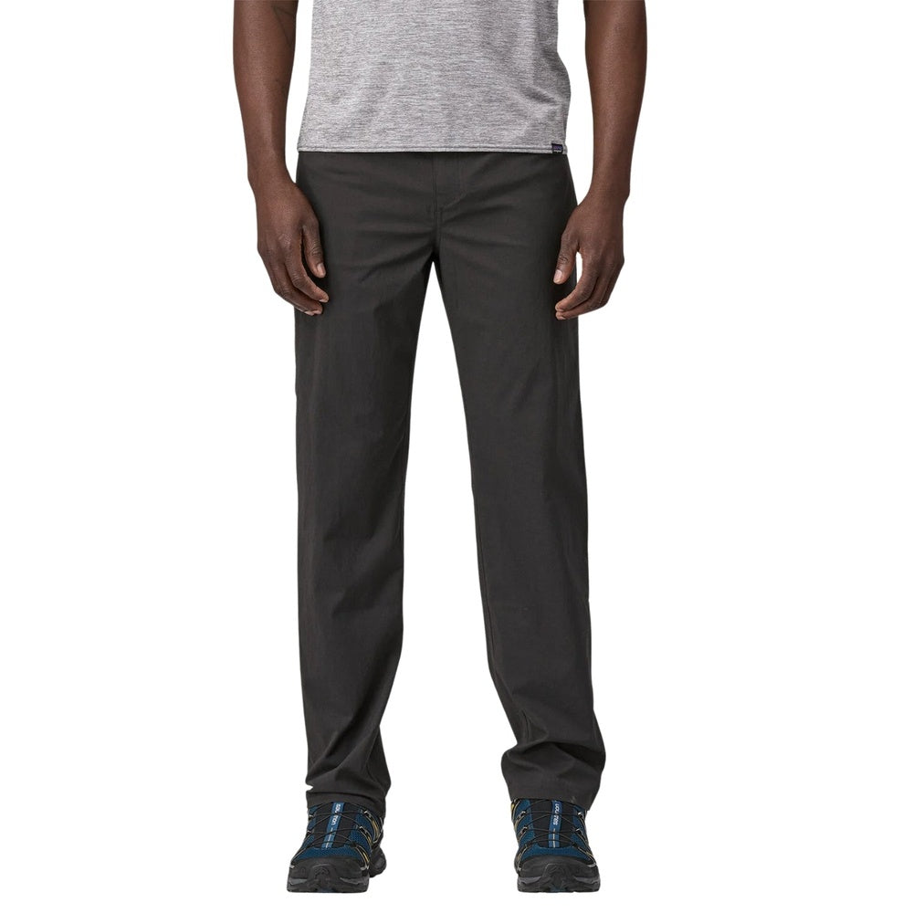Man wearing dark gray Patagonia convertible pants with hiking shoes on white background