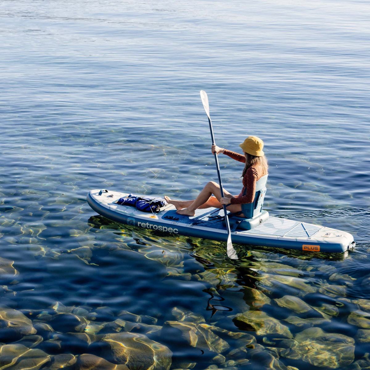 Woman paddling Retrospec Weekender Plus inflatable SUP kayak hybrid on calm clear water