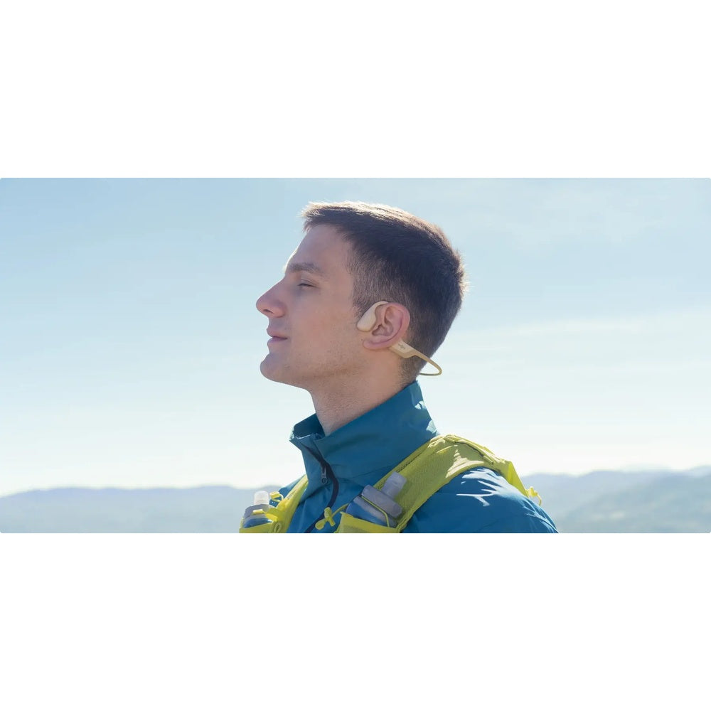 Man wearing bone conduction headphones outdoors looking toward horizon in profile view