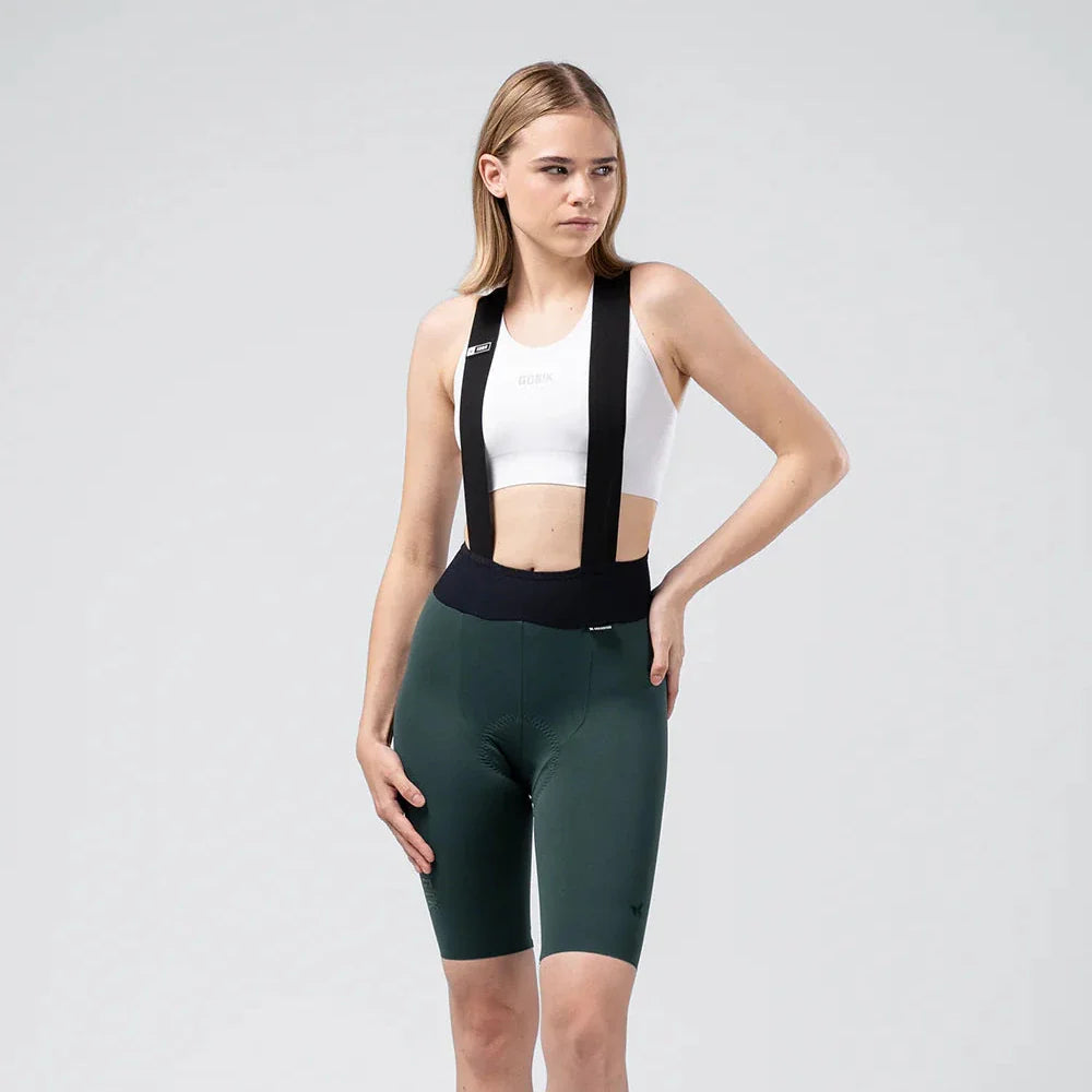 Woman wearing Gobik X dark green bib shorts with suspenders and white sports bra