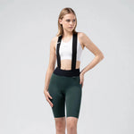 Woman wearing Gobik X bib shorts in dark green with white sports bra