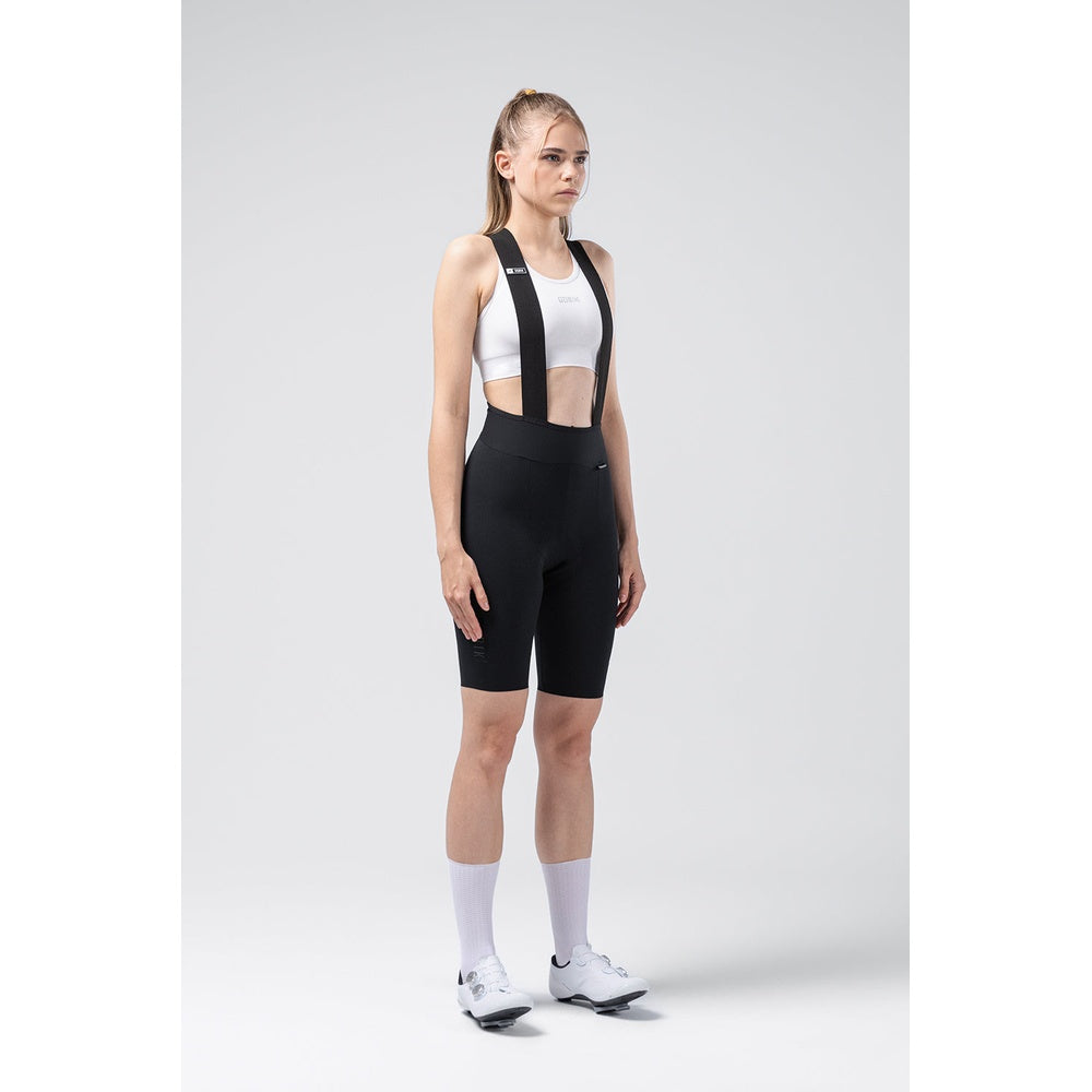 Woman wearing black Gobik X bib shorts with white sports bra in studio