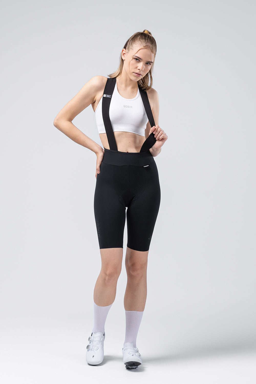 Woman wearing black Gobik X bib shorts with suspenders and white sports bra