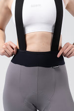 Gobik X Women's bib shorts in gray with black suspenders and white sports bra