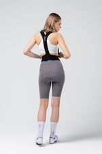 Woman wearing gray Gobik X cycling bib shorts with black suspenders, rear view