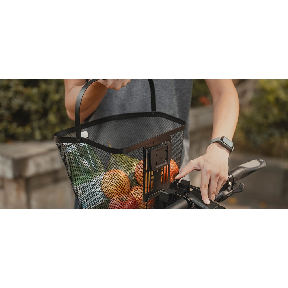 Person attaching Topeak black front mesh basket loaded with groceries onto bicycle handlebar