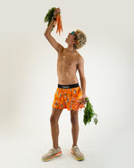 Male model wearing orange ChicknLegs Bad Bunny split shorts holding carrots overhead