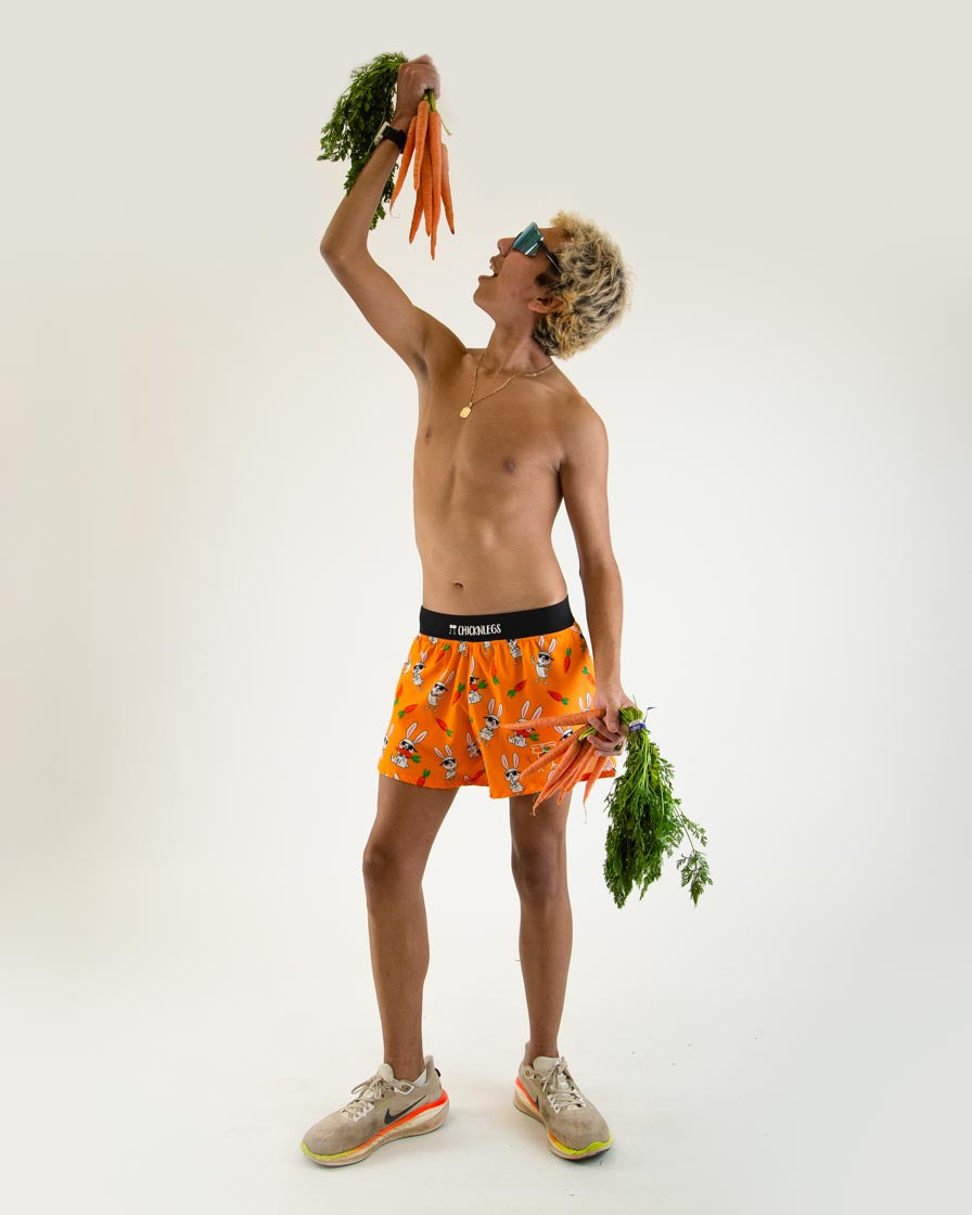 Male model wearing orange ChicknLegs Bad Bunny split shorts holding carrots overhead