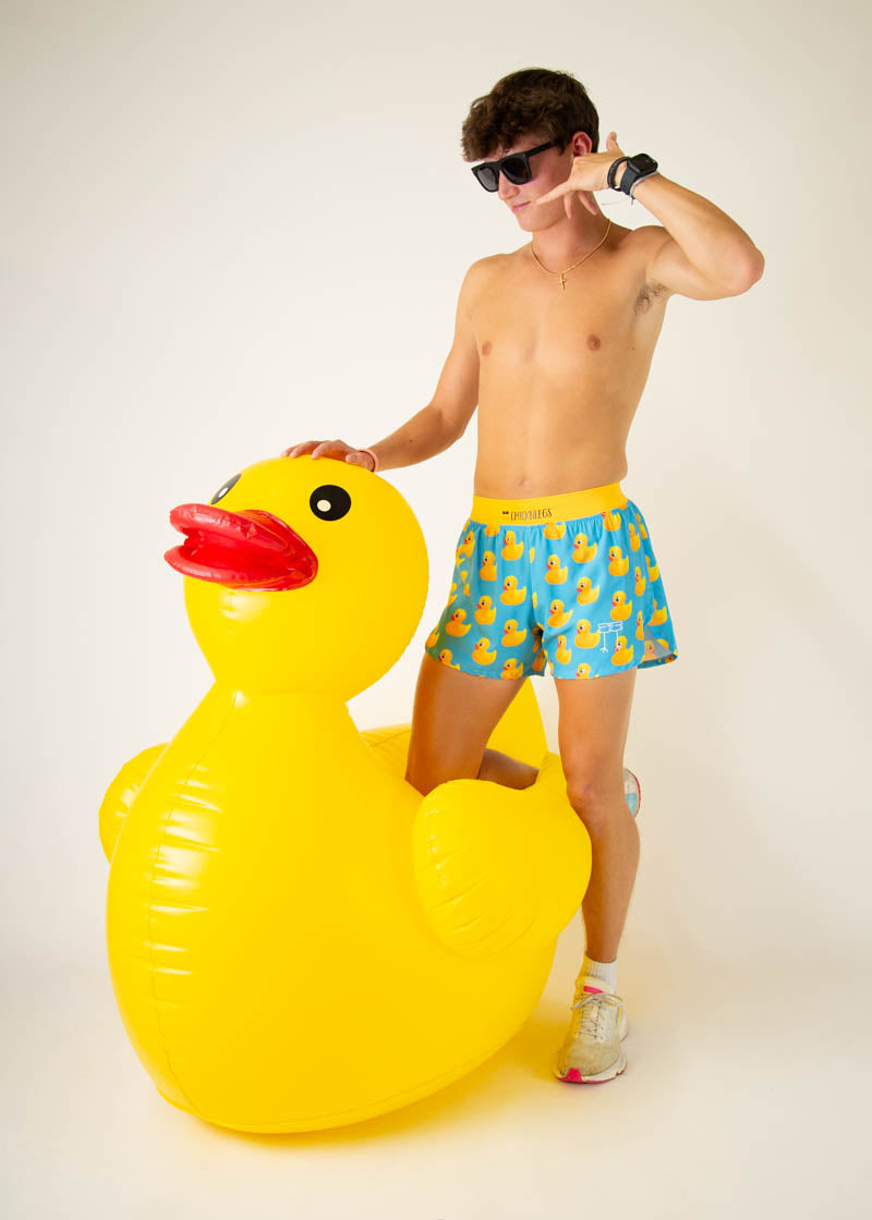 Man wearing ChicknLegs rubber ducky print swim shorts posing with inflatable duck