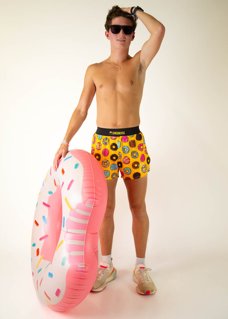 Man wearing ChicknLegs yellow donut-patterned shorts holding inflatable donut pool float