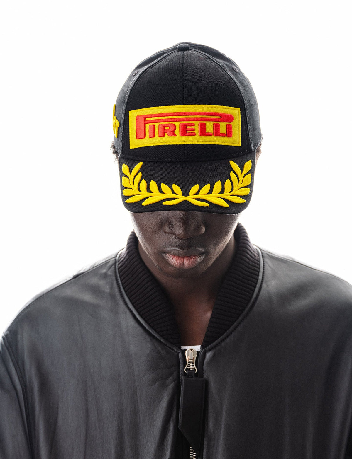 Black Pirelli snapback cap with yellow laurel wreath and embroidered logo worn by male model