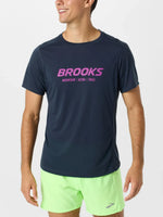 Man wearing Brooks Distance Short Sleeve 3.0 in navy blue with pink logo and green shorts