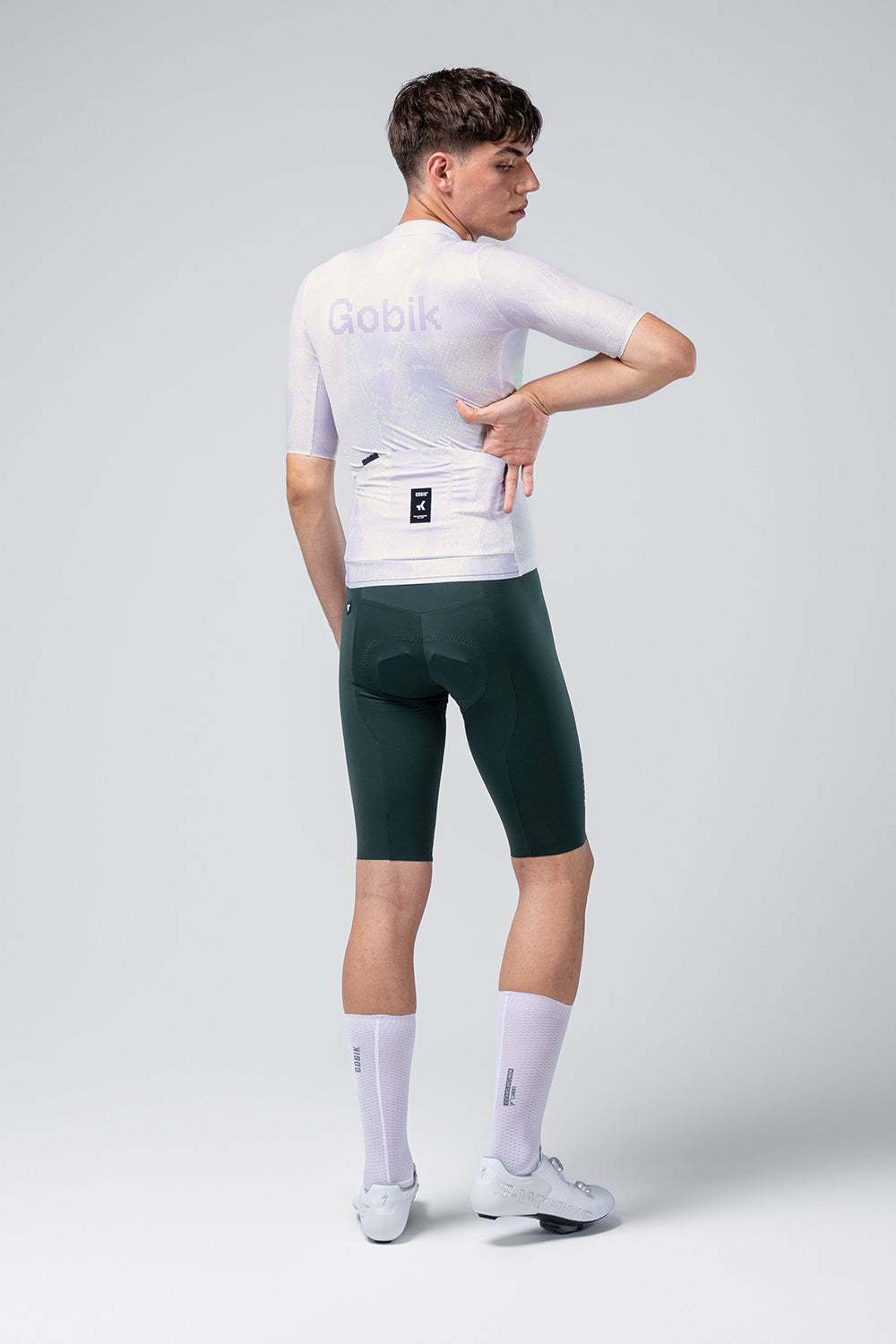 Male cyclist wearing Gobik white jersey and dark green bib shorts, rear view